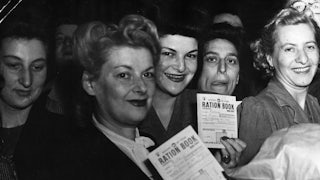Women hold up their ration books while smiling.