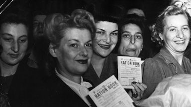 Women hold up their ration books while smiling.