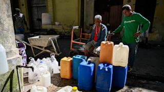 Two men on the left stand behind dozens of plastic bottles waiting to be filled with water in a street in Havana, Cuba.