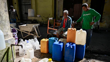 Two men on the left stand behind dozens of plastic bottles waiting to be filled with water in a street in Havana, Cuba.