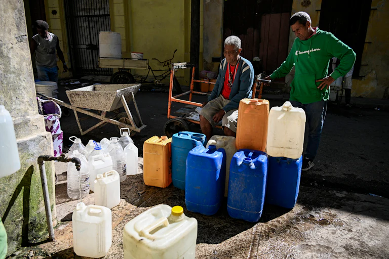 Two men on the left stand behind dozens of plastic bottles waiting to be filled with water in a street in Havana, Cuba.