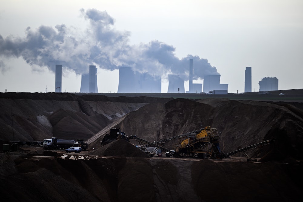 Machines work in a hole in the ground, with cooling towers emitting steam above and beyond them.