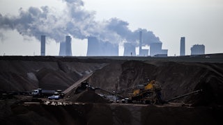 Machines work in a hole in the ground, with cooling towers emitting steam above and beyond them.