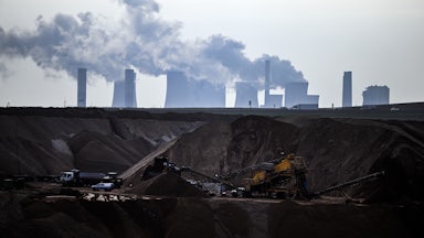 Machines work in a hole in the ground, with cooling towers emitting steam above and beyond them.