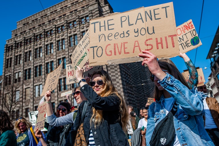 Protesters hold up signs, including one that reads: "the planet needs you to give a shit."