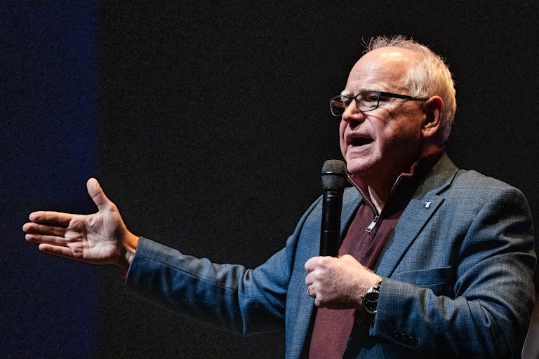 Tim Walz speaks into a microphone and holds his hand out