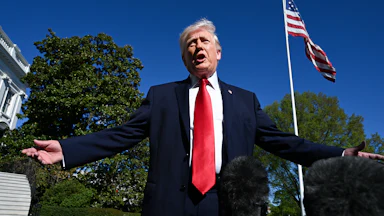 Donald Trump holds his arms out to the side and speaks while standing outside the White House