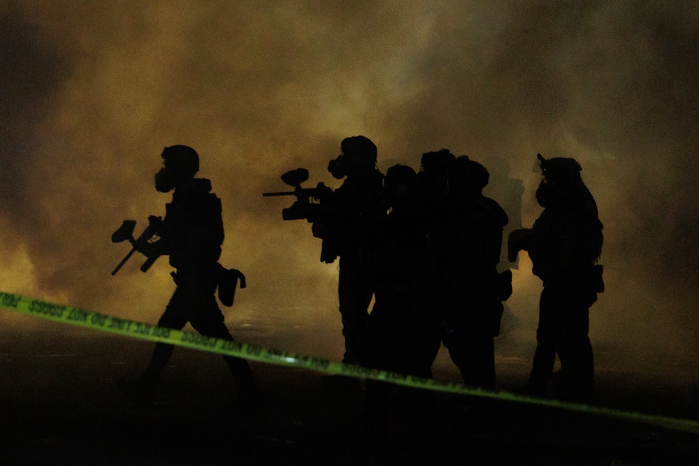 Six federal agents wearing gas masks walk through tear gas at night.