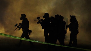 Six federal agents wearing gas masks walk through tear gas at night.