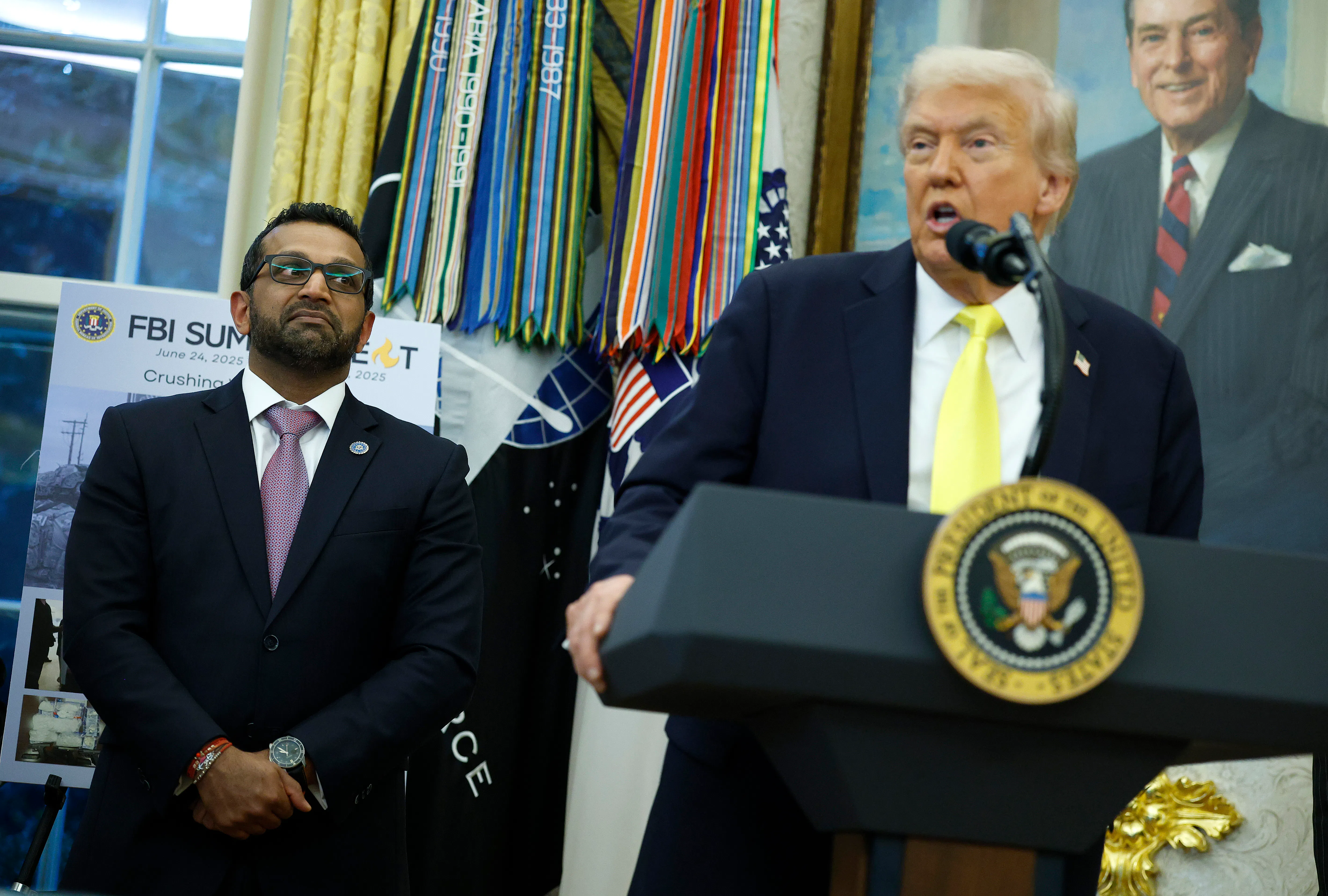 FBI Director Kash Patel stands next to Donald Trump, who speaks at a podium in the Oval Office