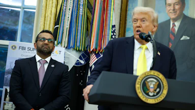 FBI Director Kash Patel stands next to Donald Trump, who speaks at a podium in the Oval Office