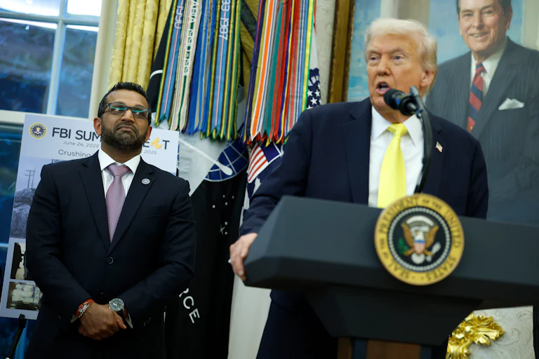 FBI Director Kash Patel stands next to Donald Trump, who speaks at a podium in the Oval Office