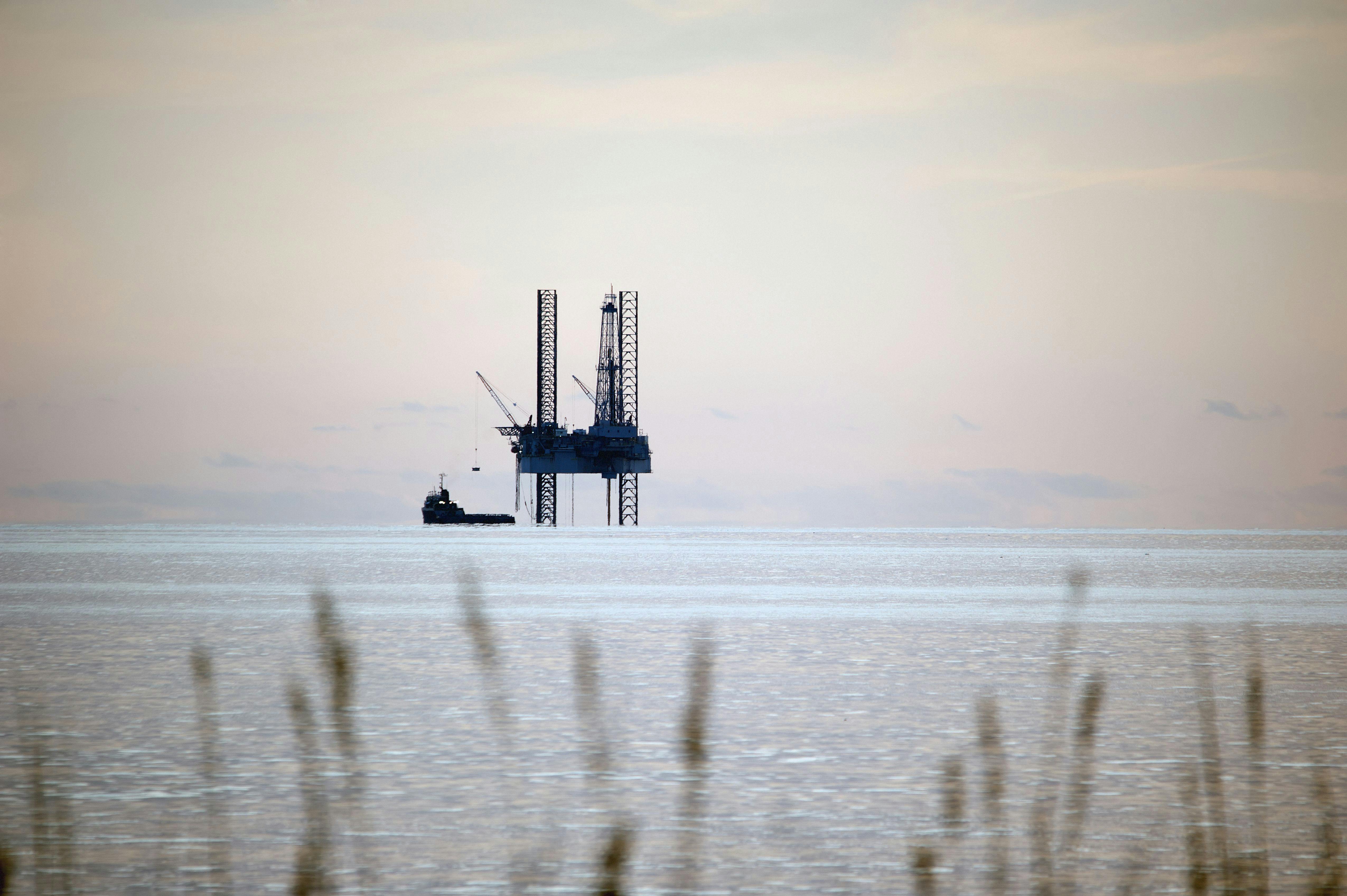 This picture shows an oil rig rising up out of the water, with marsh grasses in the foreground.