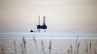 This picture shows an oil rig rising up out of the water, with marsh grasses in the foreground.
