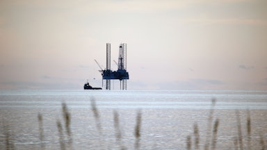 This picture shows an oil rig rising up out of the water, with marsh grasses in the foreground.