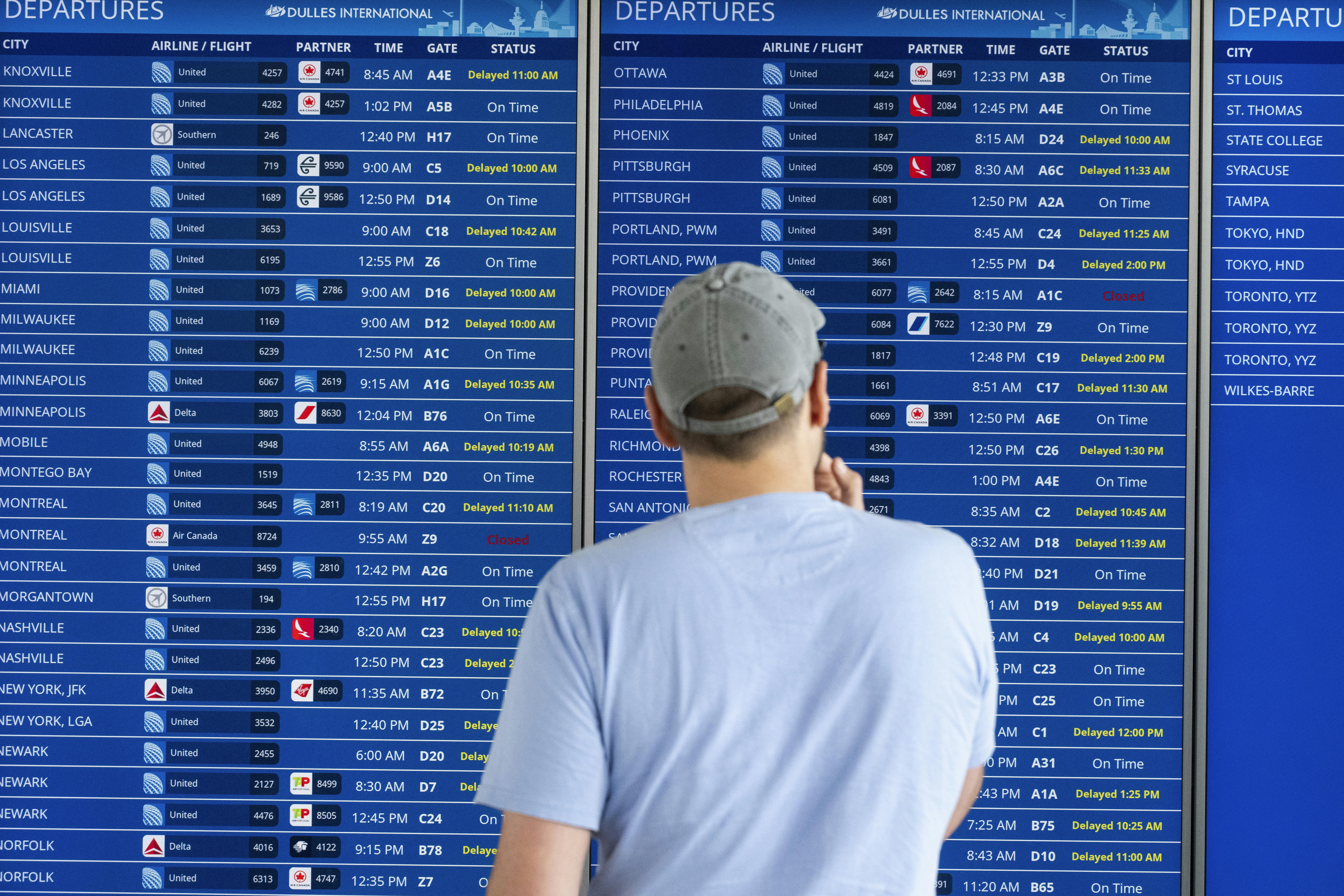 A passenger looks at a flight information board showing multiple delays and some cancellations in flight departures from Dulles International Airport.