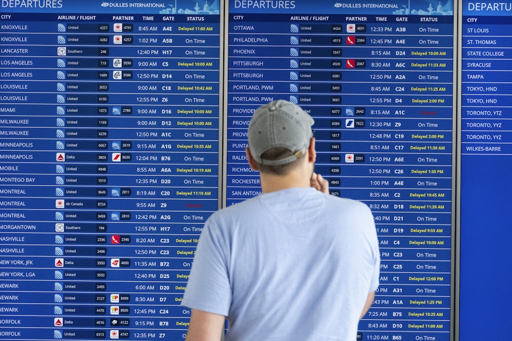 A passenger looks at a flight information board showing multiple delays and some cancellations in flight departures from Dulles International Airport.