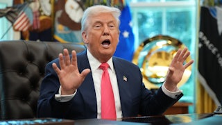 Donald Trump holds up his hands and speaks while sitting at his desk in the Oval Office