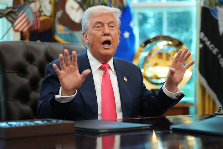 Donald Trump holds up his hands and speaks while sitting at his desk in the Oval Office