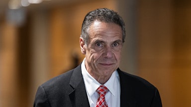 Andrew Cuomo awkwardly stares ahead as he walks through a hall