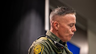 Greg Bovino looks down while wearing full camouflage