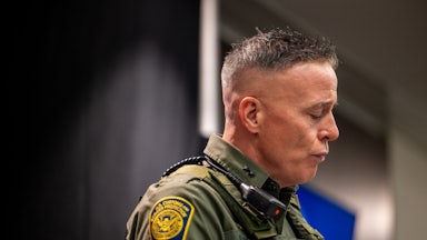 Greg Bovino looks down while wearing full camouflage