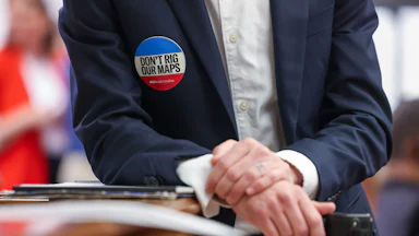 An attendee wears a “Don’t Rig Our Maps” sticker during a meeting in the Blatt Building at the South Carolina State Capitol in Columbia, South Carolina on Friday, May 8, 2026.