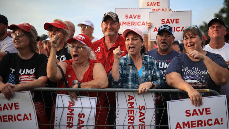 Supporters of Donald Trump cheer behind a fence, many holding "Save America" posters