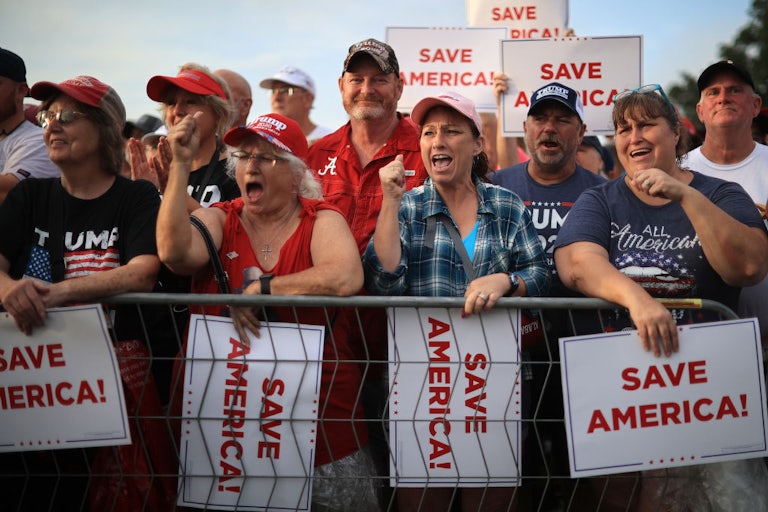 Supporters of Donald Trump cheer behind a fence, many holding "Save America" posters