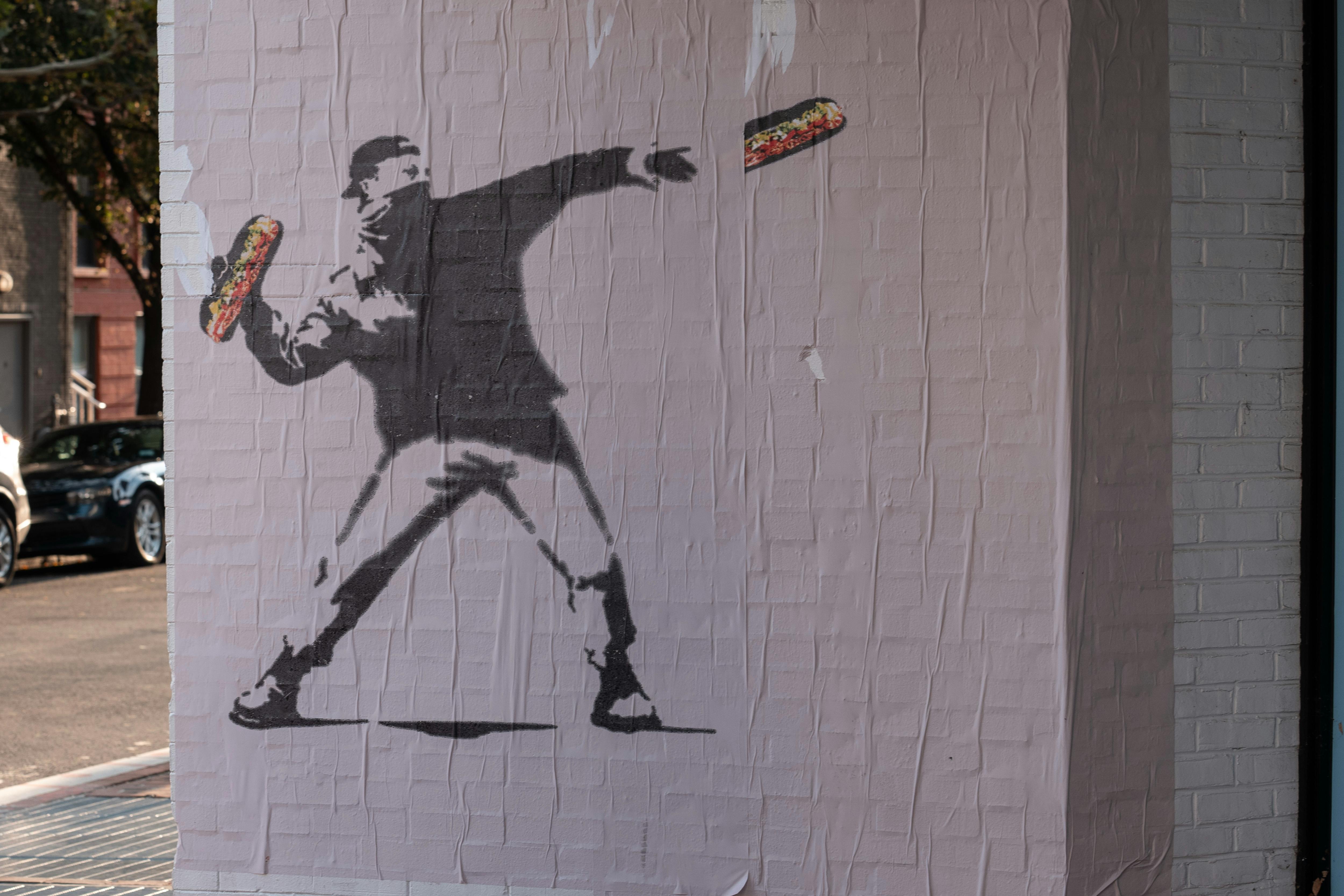 A Bansky-like mural of the D.C. sandwich guy throwing a sandwich while wearing a face mask and a backwards cap.