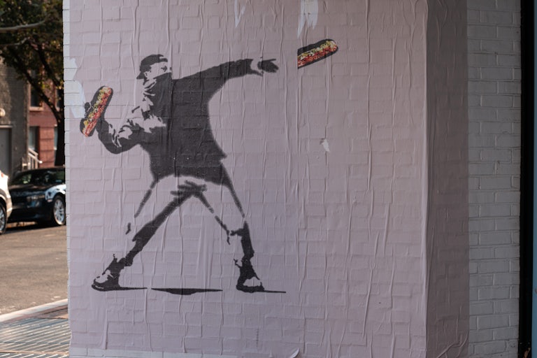 A Bansky-like mural of the D.C. sandwich guy throwing a sandwich while wearing a face mask and a backwards cap.