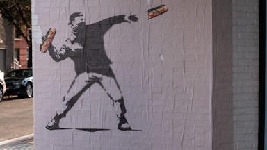 A Bansky-like mural of the D.C. sandwich guy throwing a sandwich while wearing a face mask and a backwards cap.