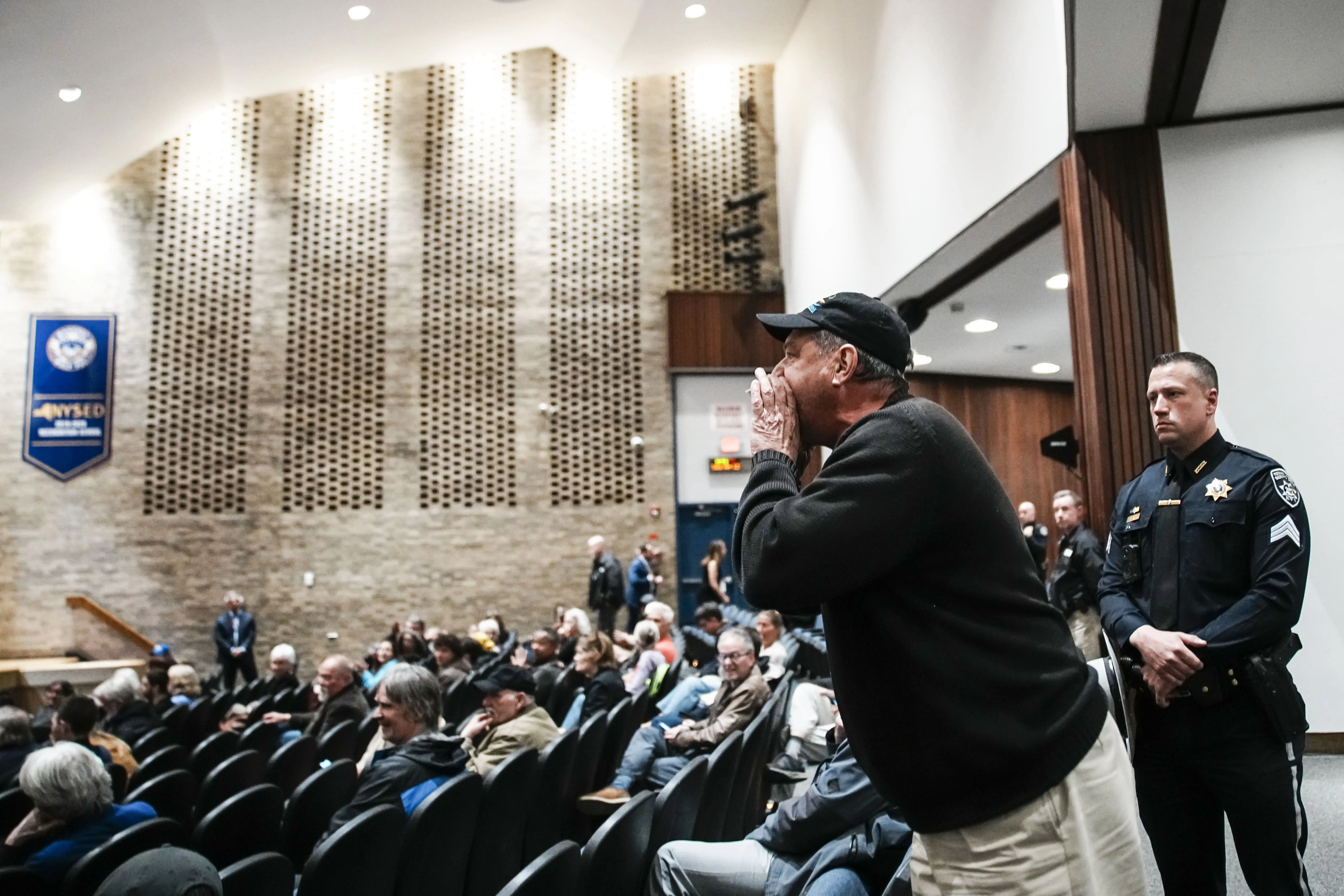 A man cups his hand as he stands and yells in Representative Mike Lawler's town hall.