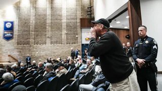 A man cups his hand as he stands and yells in Representative Mike Lawler's town hall.