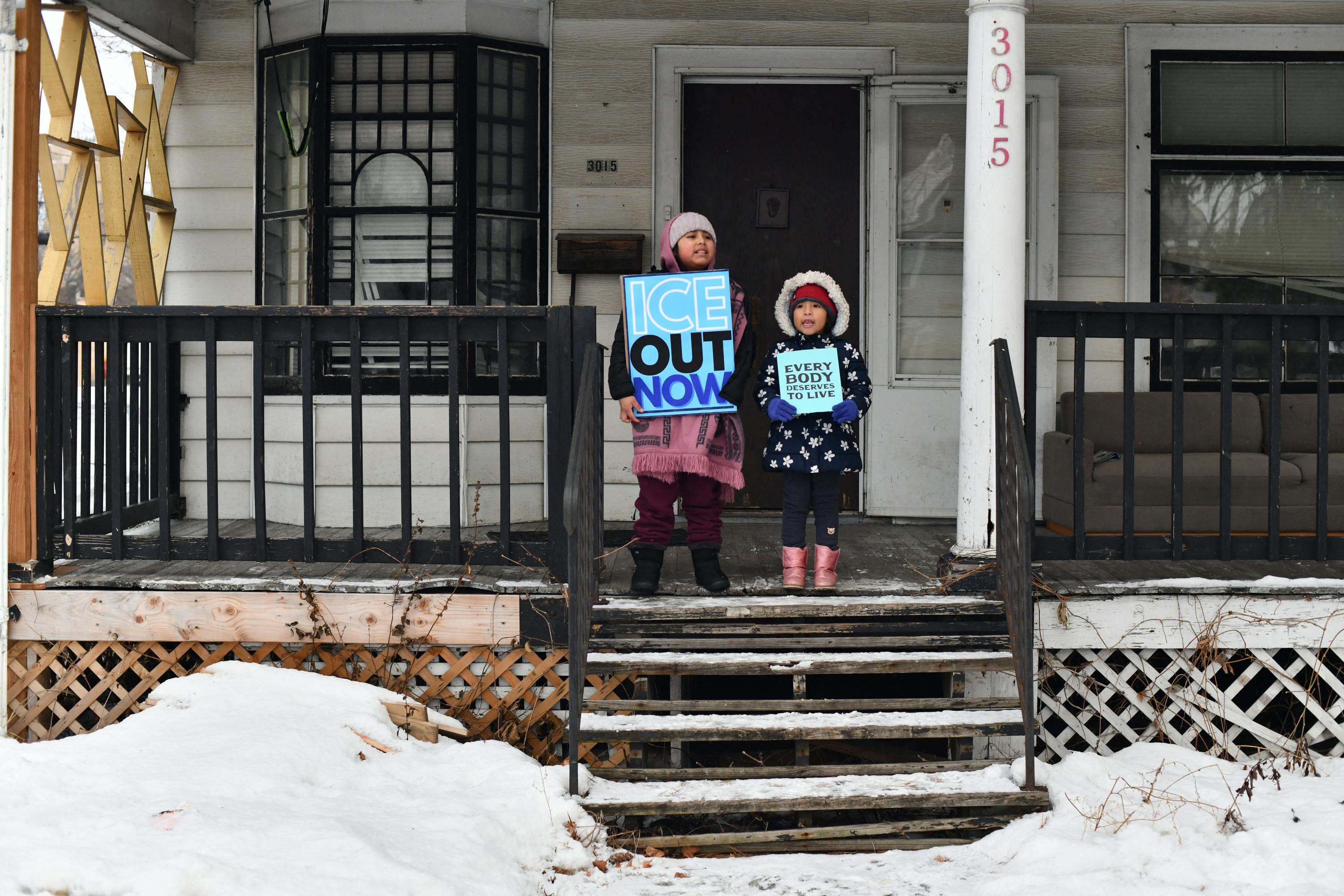 Children hold signs on the stoop of a house as protesters march from Powderhorn Park in Minneapolis against Immigration and Customs Enforcement and the fatal shooting of Renee Good.