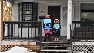 Children hold signs on the stoop of a house as protesters march from Powderhorn Park in Minneapolis against Immigration and Customs Enforcement and the fatal shooting of Renee Good.