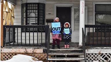 Children hold signs on the stoop of a house as protesters march from Powderhorn Park in Minneapolis against Immigration and Customs Enforcement and the fatal shooting of Renee Good.