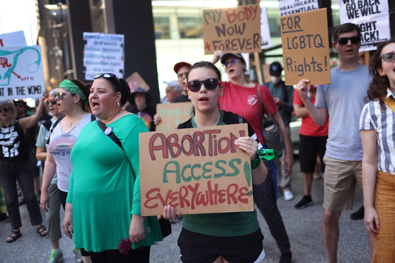 A protester holds a sign reading "Abortion Access Everywhere!" in a group featuring a number of pro-abortion and pro-LGBTQ rights signs.