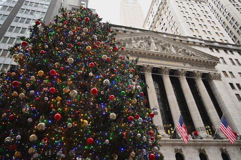 A christmas tree laden with ornaments stands in front of the ornate, columned building that houses the New York Stock Exchange.