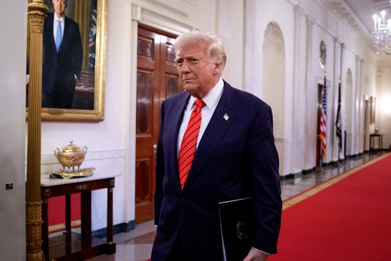 Donald Trump walks down a red carpet in the White House as he prepares to sign an executive order, which he is likely holding in his left hand.