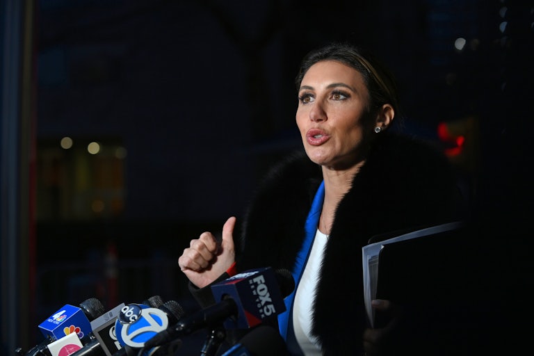 Alina Habba speaks outside at nighttime. Several press mics are in front of her.