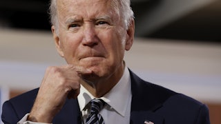 President Joe Biden strokes his chin as he grimaces.