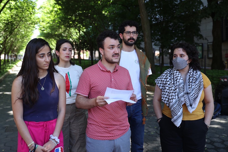 Columbia University student Mahmoud Khalil stands in the middle of 4 other people and reads something from a piece of paper in his hands.