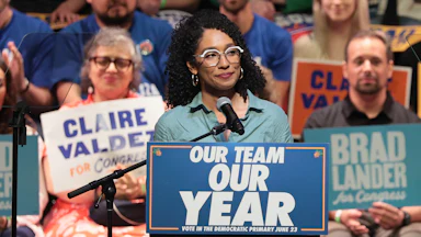 Congressional candidate Darializa Avila Chevalier stands at a podium that reads "Our Team, Our Year." Supporters in the background hold signs with the names of Claire Valdez and Brad Lander.