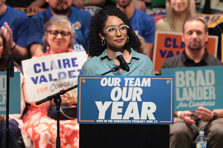 Congressional candidate Darializa Avila Chevalier stands at a podium that reads "Our Team, Our Year." Supporters in the background hold signs with the names of Claire Valdez and Brad Lander.