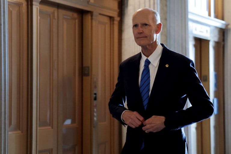 Senator Rick Scott buttons his jacket while walking in the Capitol