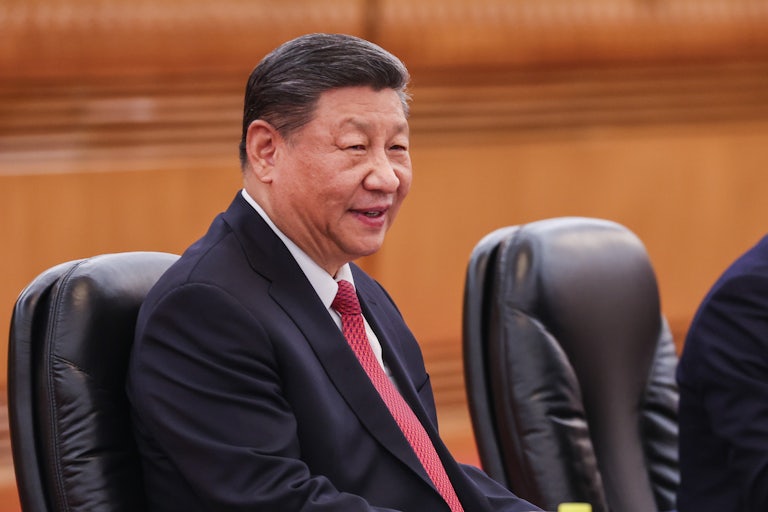 Chinese President Xi Jinping sits on a chair and smiles.
