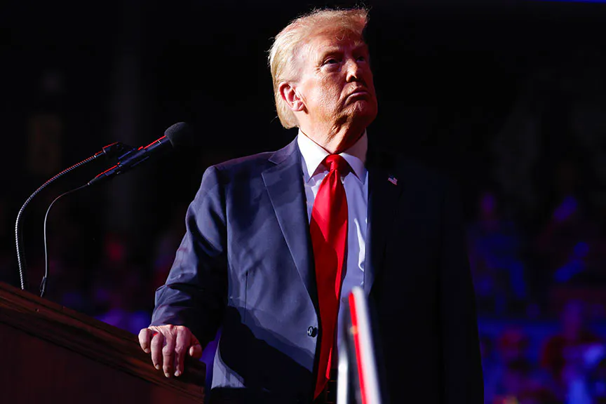 Donald Trump stands at a podium in a navy suit and red tie
