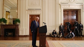 President Joe Biden stands behind a lectern, looking down at the floor.