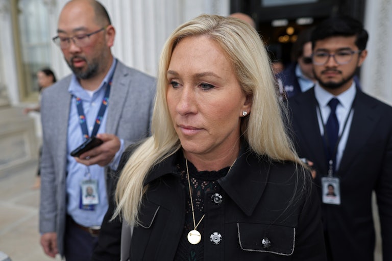 Marjorie Taylor Greene walks as two men (probably reporters) follow her